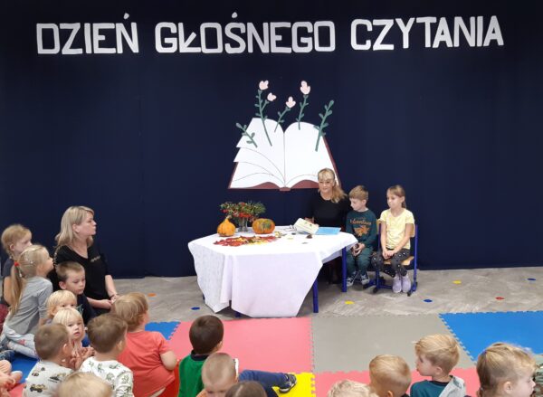 Dyrektor przedszkola razem z Oleńką i Olkiem czytają wszystkim przedszkolakom książkę w ramach obchodów Ogólnopolskiego Dnia Głośnego Czytania