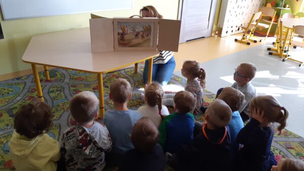 Bibliotekarka opowiada dzieciom bajkę z wykorzystaniem magicznego drewnianego teatrzyku - Kamishibai
