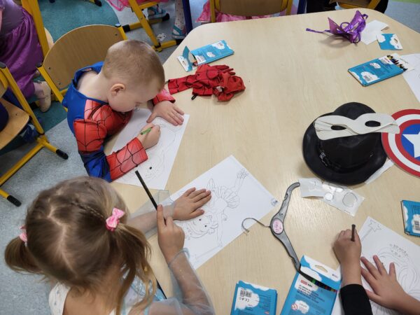 Dzieci przy stoliku kolorują postaci z bajek.