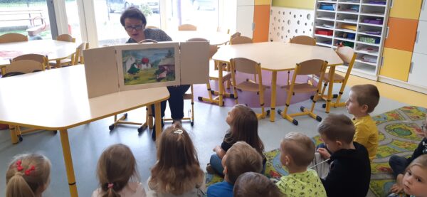 Bibliotekarka opowiada dzieciom bajkę z wykorzystaniem magicznego drewnianego teatrzyku - Kamishibai