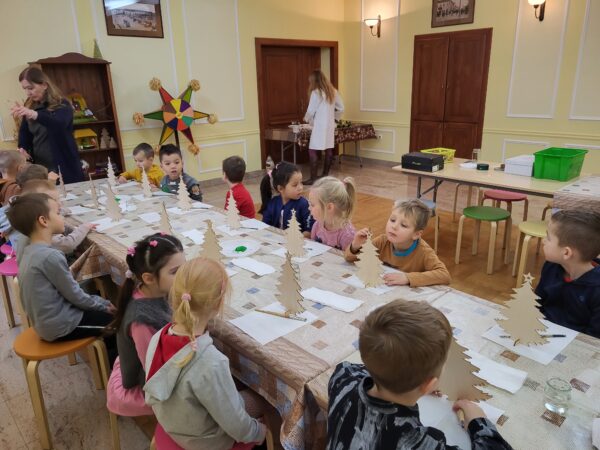 Dzieci siedzą przy stole , czekają na wykonanie choinek.