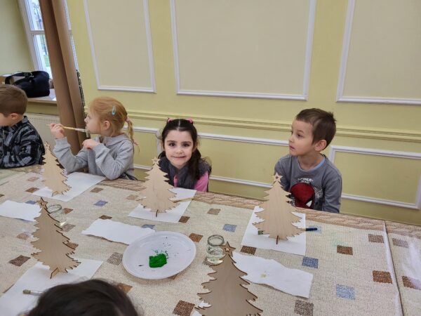 Dzieci siedzą przy stole , czekają na wykonanie choinek.