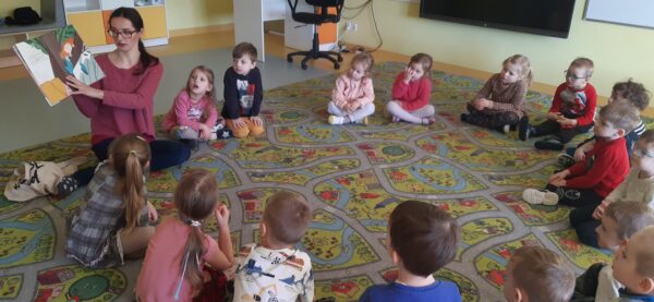 Dzieci słuchają uważnie książki czytanej przez bibliotekarkę
