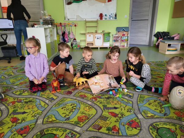 Dzieci siedzą w kole i podziwiają swoje dinozaury.
