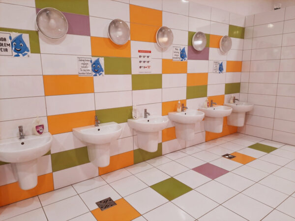 Wnętrze sanitariatów dla dzieci przedstawiajace szereg umywalek