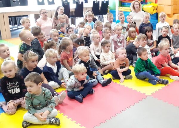 Dzieci słuchają książki czytanej przez dyrektora przedszkola, Oleńkę i Olka