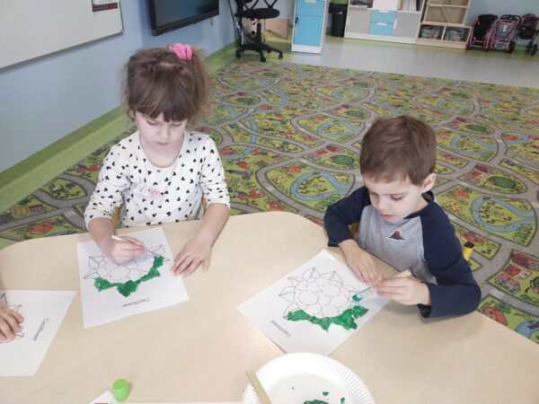 Przedszkolaki używają zielonej farby do zamalowania liści