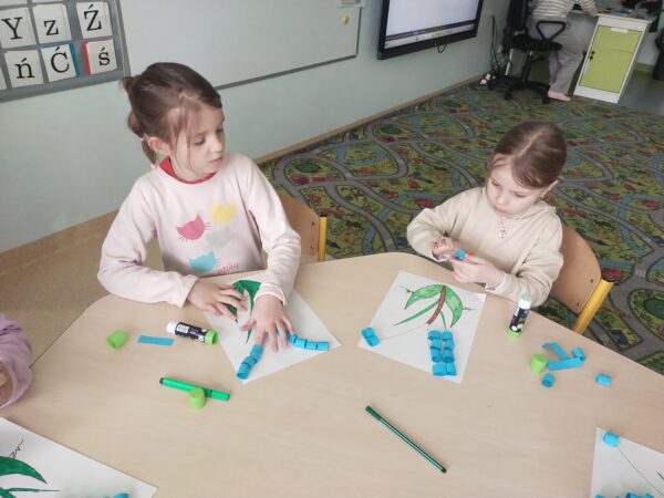 Dziewczynki starannie sklejają paski niebieskiego papieru