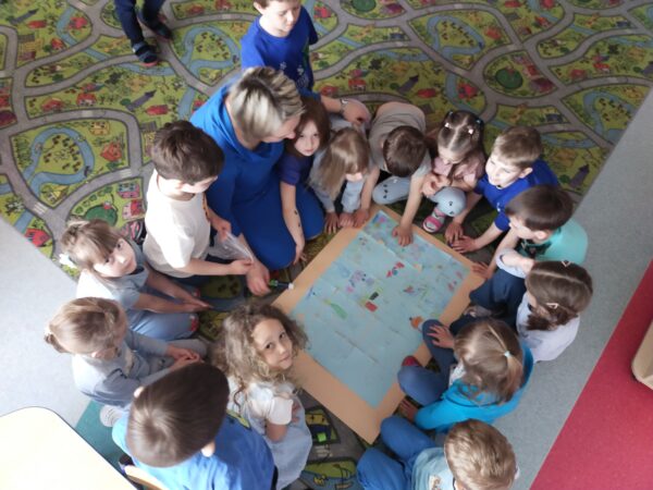 Przedszkolaki przyklejają puzzle na wspólnym plakacie