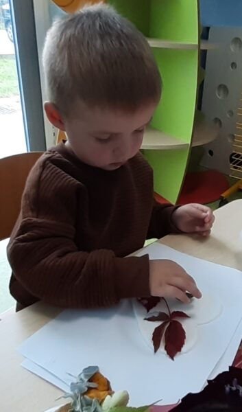 Jaś ozdabia serduszko materiałem przyrodniczym.