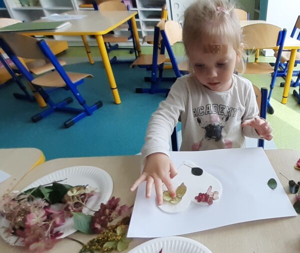 Zosieńka ozdabia serduszko materiałem przyrodniczym.