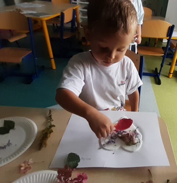 Wojtuś ozdabia serduszko materiałem przyrodniczym.