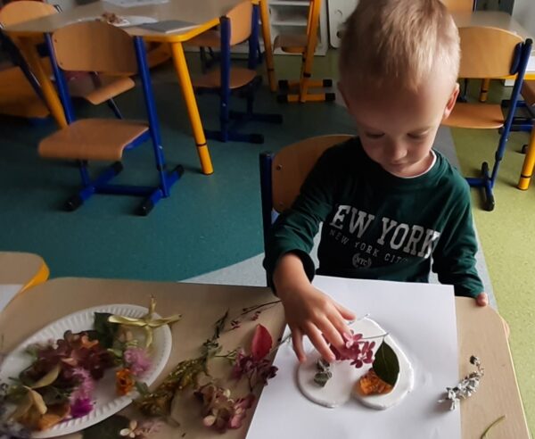 Krzyś ozdabia serduszko materiałem przyrodniczym.