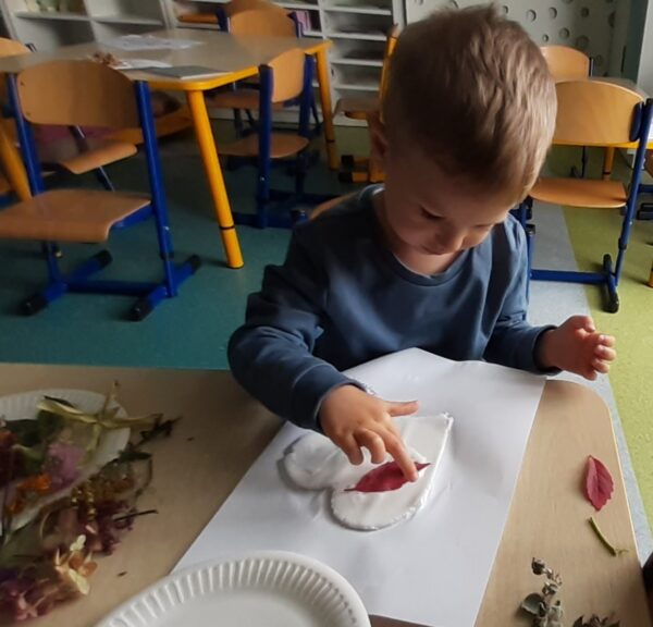 Kacperek ozdabia serduszko materiałem przyrodniczym.