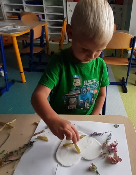 Kacperek ozdabia serduszko materiałem przyrodniczym.