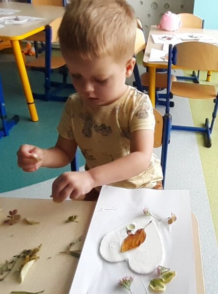 Szymonek ozdabia serduszko materiałem przyrodniczym.