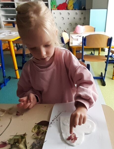 Karolcia ozdabia serduszko materiałem przyrodniczym.