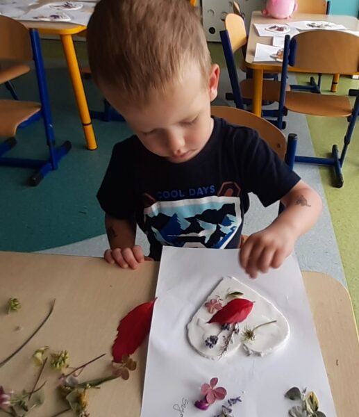 Szymonek ozdabia serduszko materiałem przyrodniczym.