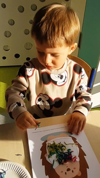 Franek wykonuje pracę plastyczną z wykorzystaniem różnorodnych faktur włóczki.